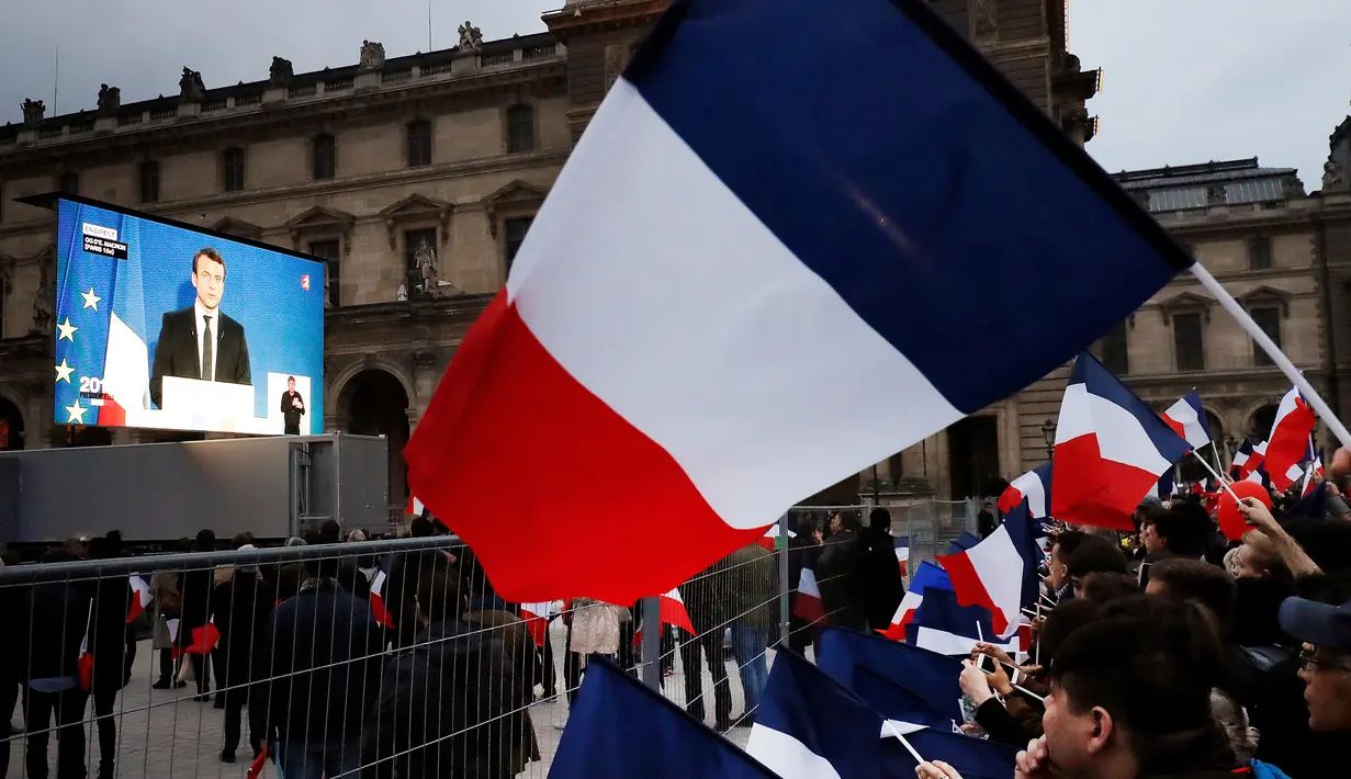 Para pendukung menonton pidato kemenangan Emmanuel Macron di luar museum Louvre, Paris, Minggu (7/5). Macron menjadi presiden Prancis setelah telak mengalahkan rivalnya Marine Le Pen dalam Pilpres Prancis putaran kedua. (Patrick KOVARIK / AFP)