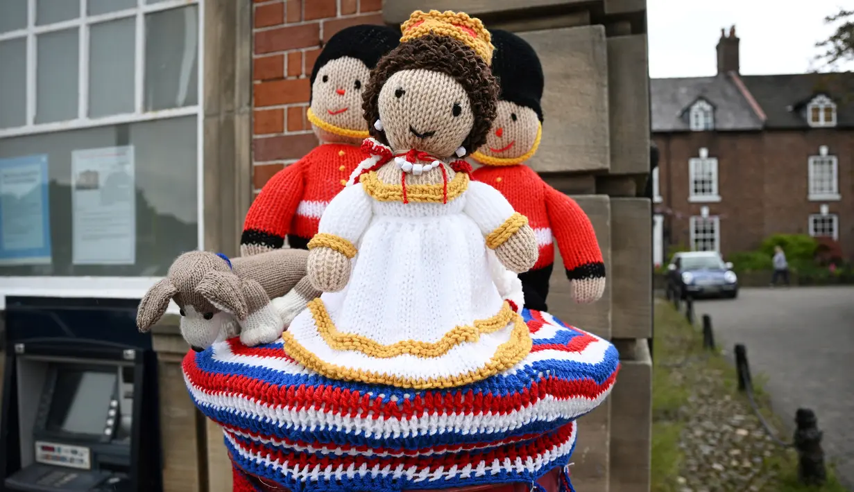 Rajutan berbentuk Ratu Elizabeth II dan pengawal Inggris dipajang di atas kotak pilar Royal Mail di Kapel Holmes, barat laut Inggris, pada 30 Mei 2022. Sebuah kelompok masyarakat lokal, The Holmes Chapel Community Yarn Bombers telah memenuhi desa dengan barang-barang rajutan patriotik untuk merayakan Platinum Jubilee Ratu. (Paulus ELLIS / AFP)