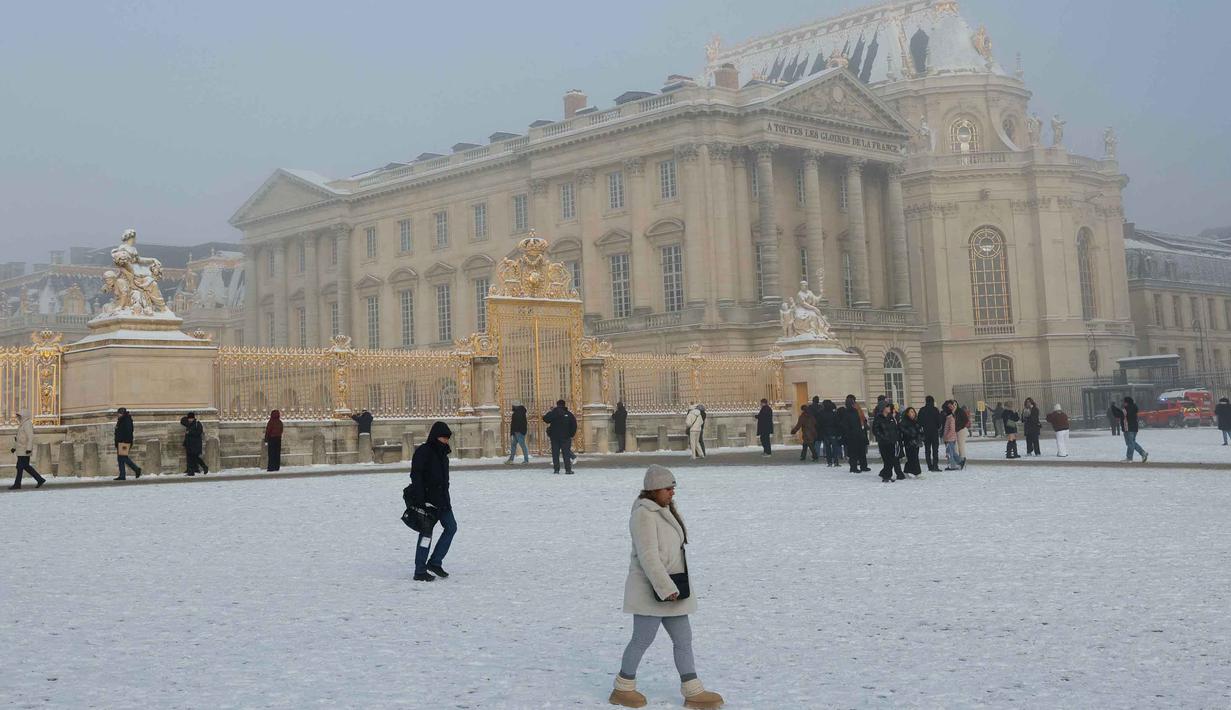 Salju yang menumpuk di atas permukaan jalan yang membeku membuat akses transportasi menjadi licin. Tampak dalam foto, para pengunjung melewati Chateau de Versailles yang diselimuti salju, di Versailles, luar Kota Paris pada Selasa 6 Januari 2026. (GEOFFROY VAN DER HASSELT/AFP)