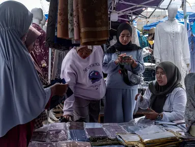 Pembeli berjalan di antara kios-kios penjual pakaian lokal di salah satu pasar tradisional, Jakarta, Kamis 20 November 2025. Sempat mengalami guncangan akibat maraknya produk impor dengan harga yang sangat murah, industri tekstil nasional mendapat titik terang. (BAY ISMOYO/AFP)