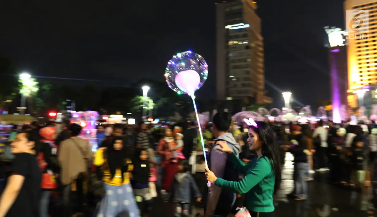 Warga membawa balon saat car free night pada malam pergantian tahun di Jalan MH Thamrin, Jakarta, Senin (31/12). Hujan yang mengguyur Jakarta sejak siang tidak menyurutkan antusias warga menikmati car free night. (Liputan6.com/Angga Yuniar)