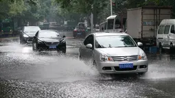 Mobil-mobil melintas di sebuah jalan yang tergenang air di Distrik Xicheng, Beijing, ibu kota China (12/8/2020). Badan meteorologi Beijing mengeluarkan peringatan siaga kuning untuk hujan badai. (Xinhua/Ju Huanzong)