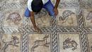 Seorang pria menggunakan kuas untuk membersihkan mosaik era Bizantium yang ditemukan di Bureij, Jalur Gaza, Palestina, 18 September 2022. Seorang petani Palestina menemukan mosaik lantai Bizantium berornamen ketika mencoba menanam pohon zaitun di tanahnya di Jalur Gaza. (MOHAMMED ABED/AFP)