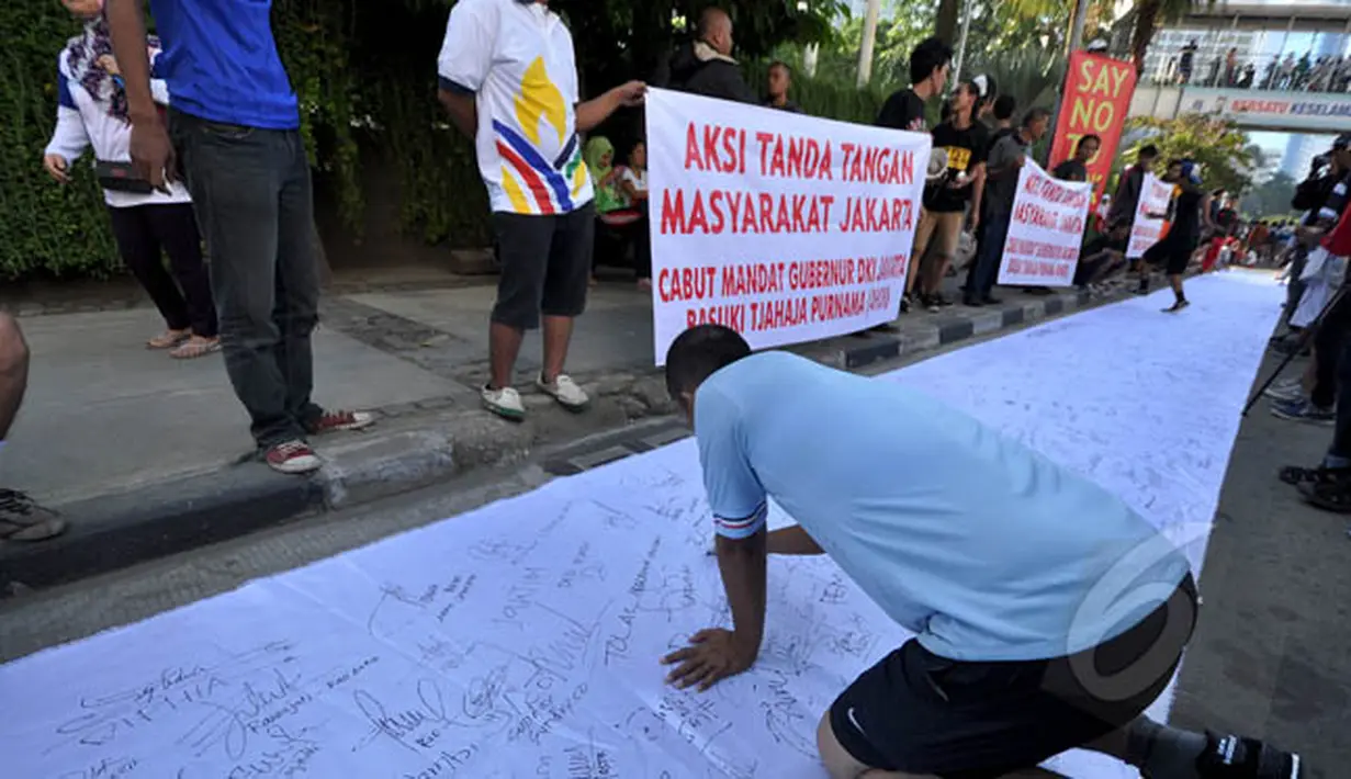 Seorang warga membubuhkan tanda tangan mendukung pemakzulan Gubernur DKI Basuki Tjahaja Purnama alias Ahok di Bundaran HI, Jakarta, Minggu (22/2/2015). Mereka melakukan aksi ini karena kebijakan Ahok dinilai tak pro-rakyat. (Liputan6.com/Faizal Fanani)