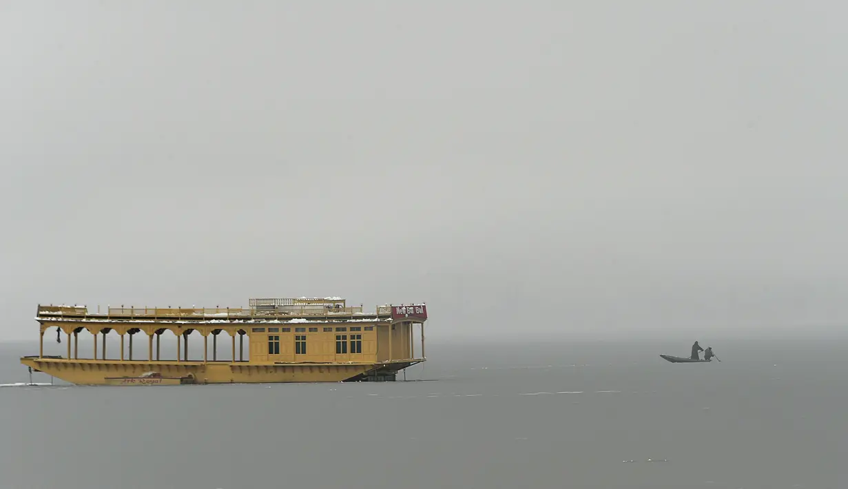 Dua pria menaiki perahu di dekat bagian beku danau Dal setelah hujan salju lebat di Srinagar (16/1/2020). Banyak daerah terpencil di lembah telah terputus akibat hujan salju lebat tersebut. (AFP Photo/Tauseef Mustafa)