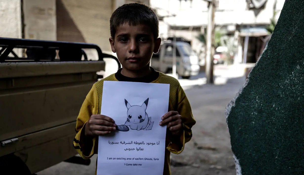 Seorang bocah memegang kertas bergambarkan karakter Pokemon dengan tulisan "Aku di Ghouta Timur di Suriah, datang dan selamatkan Aku", Suriah (22/7). (REUTERS)