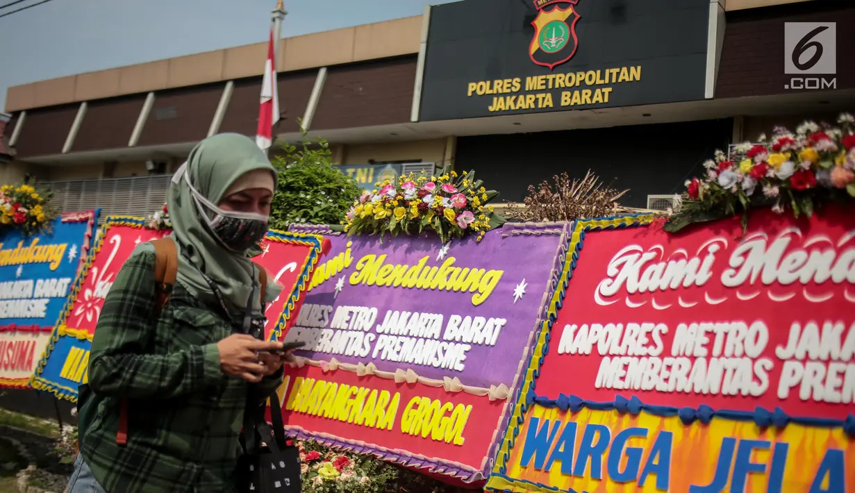 Warga melintasi karangan bunga di Halaman Polres Jakarta Barat, Jumat (23/11). Puluhan karangan bunga yang dikirimkan warga tersebut diberikan guna mendukung pihak kepolisian dalam memberantas aksi premanisme di Jakarta Barat. (Liputan6.com/Faizal Fanani)