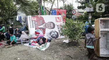 Warga korban kebakaran terlihat beristirahat dekat banner calon anggota legislatif (caleg) di Jalan Manggarai II, Tebet, Jakarta Selatan, Minggu (17/12/2023). (Liputan6.com/Faizal Fanani)