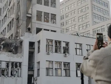 Seseorang mengambil foto gedung Derzhprom—sebuah gedung pencakar langit bersejarah Soviet—yang rusak setelah serangan rudal di Kharkiv pada 29 Oktober 2024. (Ivan SAMOILOV/AFP)