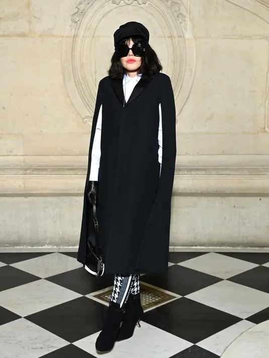Aktris Isabelle Adjani mengenakan jubah sutra dan wol hitam Dior, kemeja katun putih, dan legging bermotif houndstooth Cruise 2022. Dia juga mengenakan tas Dior Hobo, sarung tangan, kacamata hitam dan sepatu. (Dior)
