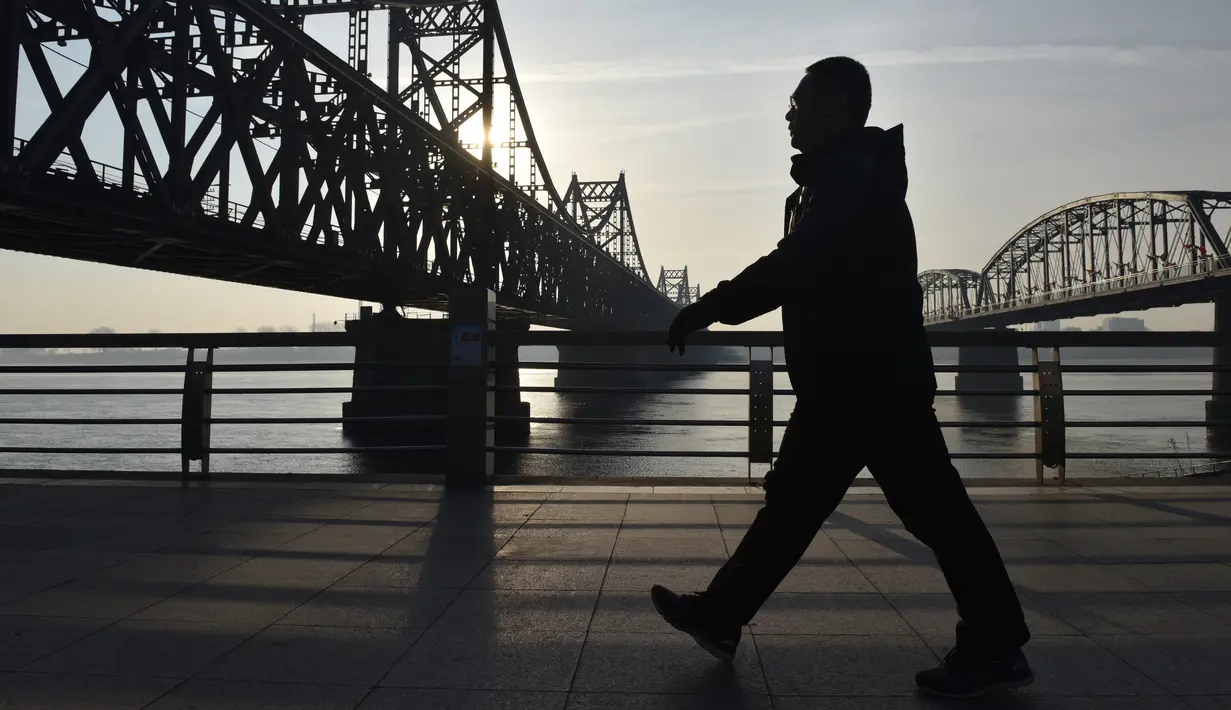Seorang pria berjalan di bawah Jembatan Persahabatan di kota Dandong di provinsi Liaoning, China (22/2). Jembatan Persahabatan ini dibangun oleh Jepang antara April 1937 dan Mei 1943. (AFP Photo/Greg Baker)