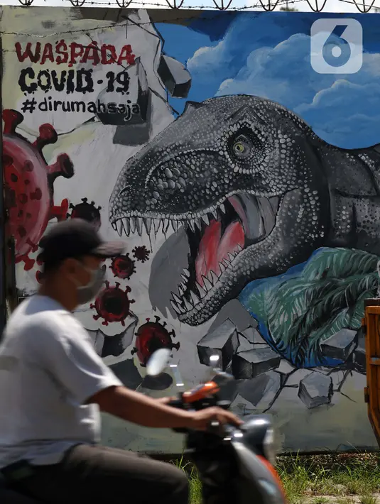 Pengendara motor melintas di depan mural bertema waspada COVID-19 di Jalan Baru, Depok, Jawa Barat, Selasa (7/4/2020). Mural tersebut berisi pesan kepada warga agar selalu waspada potensi penyebaran virus corona atau COVID-19. (Liputan6.com/Helmi Fithriansyah)