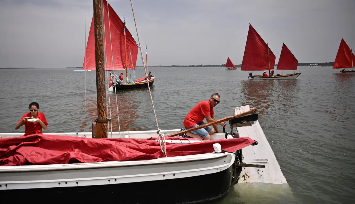 Anggota asosiasi pelayaran budaya mengambil bagian dalam acara Regatta Merah di Venesia, Italia, Minggu (20/6/2021). Red Regatta mengumpulkan lebih dari 50 perahu tradisional Venesia dengan 52 layar warna merah. (MARCO BERTORELLO/AFP)