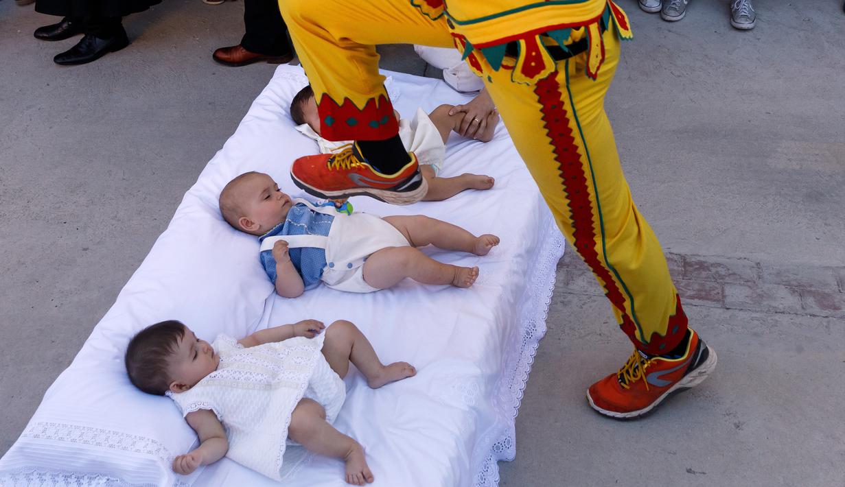 Pria berkostum setan melompati bayi-bayi yang terlentang di atas matras di sebuah jalan selama festival El Colacho di desa Castrillo de Murcia, Spanyol, Minggu (18/6). Festival melompati bayi ini sudah menjadi perayaan tahunan sejak 1620 (CESAR MANSO/AFP)