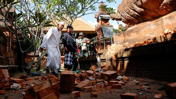 Pemuka agama dan prajurit TNI memantau kerusakan pada bagian candi yang runtuh akibat gempa di Pura Lokanatha, Denpasar, Bali, Selasa (16/7/2019). Gempa Magnitudo 5,8  yang mengguncang Bali dilaporkan terasa hingga ke Lombok dan wilayah Jawa Timur. (AP/Firdia Lisnawati)
