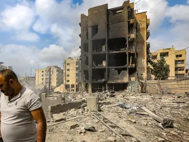 Seorang pria berjalan melewati sebuah lubang di mana sebuah bangunan yang runtuh berdiri setelah serangan udara Israel semalam di lingkungan Kafaat di pinggiran selatan Beirut, pada 7 Oktober 2024. (Foto oleh AFP)