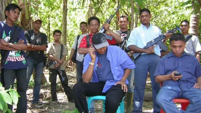 Jamaluddin memangku senapan mengenakan baju putih berdiri di antara Muzakir Manaf dan Irwandi Yusuf