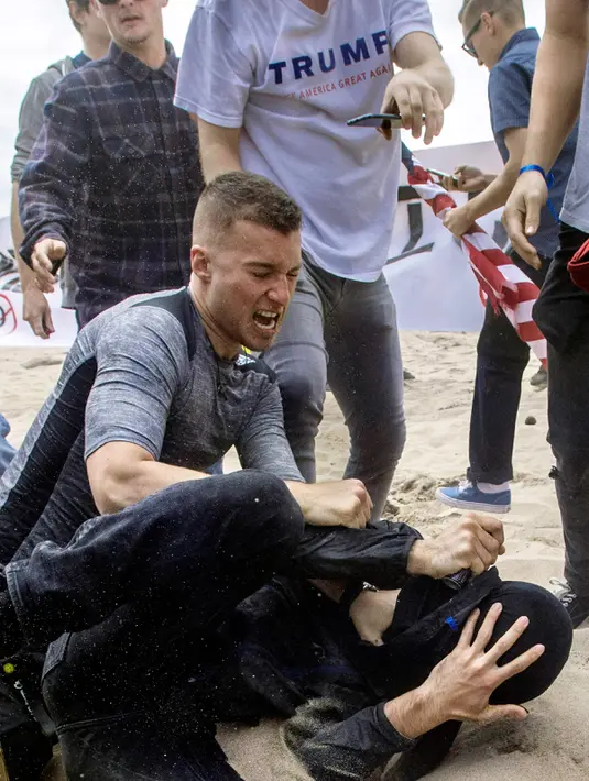 Seorang pendukung Presiden Donald Trump berkelahi dengan pengunjuk rasa anti-Trump di Huntington Beach, California (25/3). Akibat bentrokan itu beberapa orang cidera dan ditangkap pihak keamanan. (Mindy Schauer / The Orange County Register via AP)