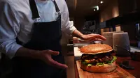 Chef dari restoran The Oak Door, Patrick Shimada berpose dengan burger raksasa di hotel Grand Hyatt Tokyo, Senin (1/4). Hamburger ini memiliki diameter 25 centimeter dan berisi foie gras, daging sapi Jepang, dan jamur truffle hitam segar. (CHARLY TRIBALLEAU/AFP)