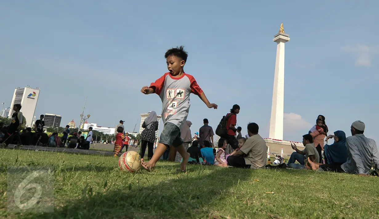 Seorang anak bermain bola di halaman Munomen Nasional (Monas), Jakarta, Kamis (7/7). Libur kedua Lebaran dimanfaatkan warga untuk bekunjung ke lokasi wisata bersama keluarga. (Liputan6.com/Yoppy Renato)