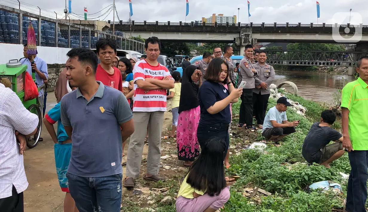 Warga bersama personel kepolisian berkumpul di bantaran Sungai Ciliwung, Jakarta, Selasa (25/2/2020). Adanya seorang warga yang hanyut saat berenang di tengah luapan Sungai Ciliwung tersebut mengundang perhatian warga serta petugas yang mencari keberadannya. (Liputan6.com/Immanuel Antonius)