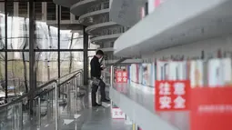 Seorang pria berdiri di dekat rak buku yang berada di dalam Perpustakaan Binhai Tianjin di China (14/11). Perpustakaan ini memiliki desain futuristik, dengan interior serba putih dan rak susun melingkar. (AFP/Fred Dufour)