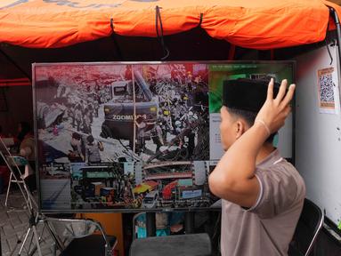Seorang santri berjalan melewati layar TV yang menayangkan upaya pencarian korban hilang dari reruntuhan bangunan di sebuah pondok pesantren di Sidoarjo, Jawa Timur, Sabtu 4 Oktober 2025. (AP Photo/Achmad Ibrahim)