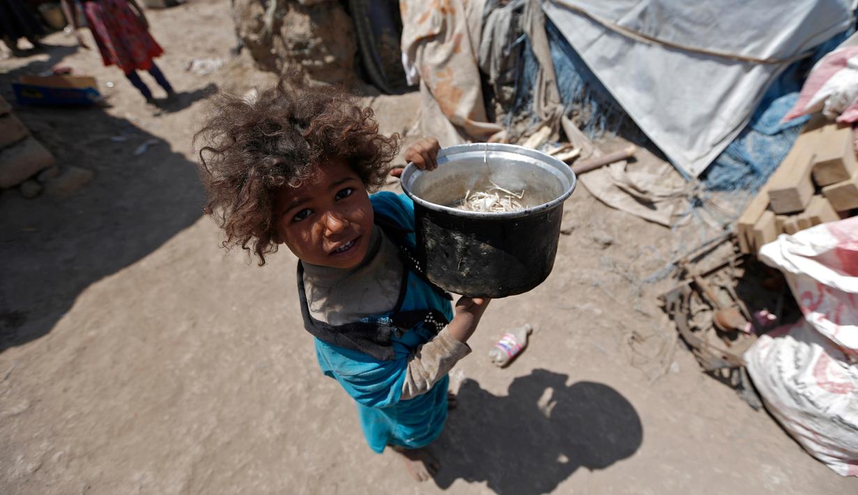 Seorang anak membawa panci saat berada dekat tenda tempat tinggalnya di kamp pengungsian di Sanaa, Yaman, (15/4). Mereka mengungsi akibat konflik di negaranya yang belum terseleasikan (AFP Photo / Mohammed Huwais)