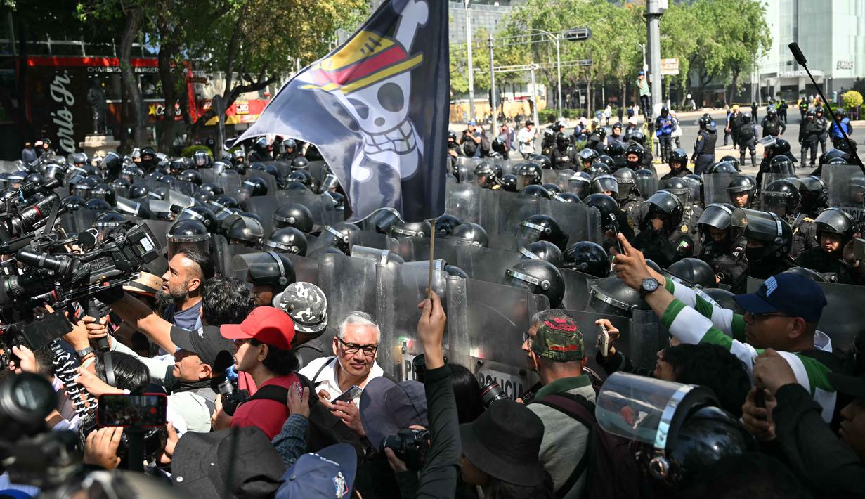 Dalam aksinya, pengunjuk rasa mengecam Presiden Claudia Sheinbaum dan menuduh pemerintah membiarkan kekerasan, korupsi, dan kartel. Tampak dalam foto, seorang pengunjuk rasa memegang bendera berlogo manga populer Jepang, One Piece, simbol yang diadopsi oleh gerakan protes Gen Z di seluruh dunia, di depan barisan polisi di sepanjang Reforma Avenue dalam sebuah demonstrasi yang dilakukan oleh anak muda Meksiko terkait dengan gelombang protes global Generasi Z terhadap pemerintahan Presiden Meksiko, Claudia Sheinbaum, di Mexico City, pada 20 November 2025. (Yuri CORTEZ/AFP)