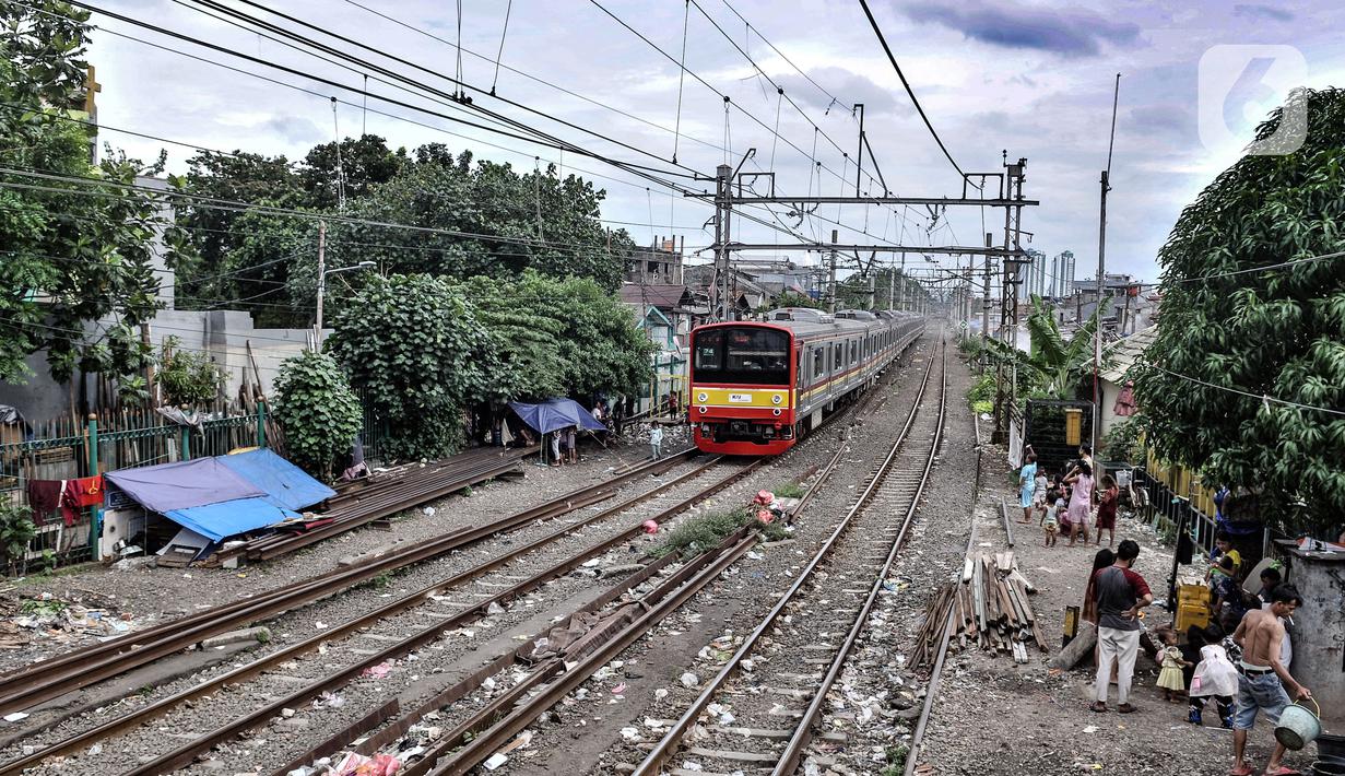 Kereta commuterline melintas di dekat deretan bangunan semipermanen milik tunawisma di kawasan Senen, Jakarta, Minggu (14/2/2021). Aminah (58) sadar tinggal di pinggir rel akan dapat mengancam nyawanya. (merdeka.com/Iqbal S. Nugroho)