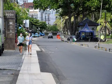 Pejalan kaki berjalan di sepanjang jalan utama yang sepi saat Pemberlakuan Pembatasan Kegiatan Masyarakat (PPKM) Level 3 di Kuta, Badung, Bali, Jumat (23/7/2021). Pemprov Bali tengah menerapkan PPKM Level 3. (SONNY TUMBELAKA/AFP)