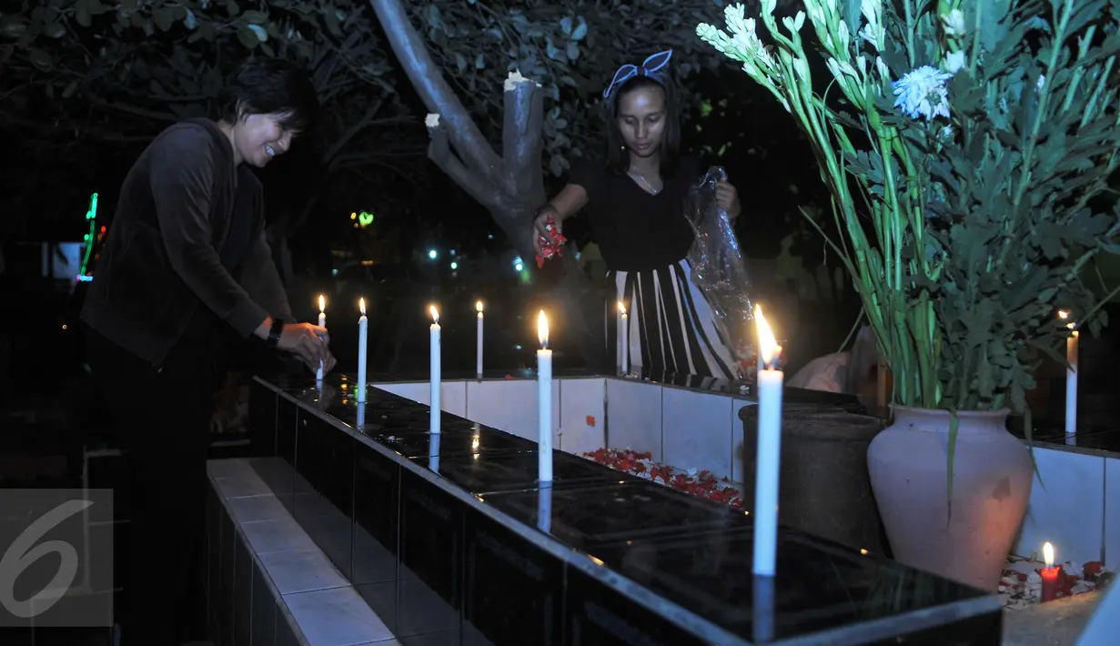 Warga menabur bunga dan menyalakan lilin saat ziarah ke makam yang terdapat di sebelah Gereja Tugu, Jakarta, Kamis (24/12). Tradisi tersebut dilakukan usai mengikuti ibadah kebaktian malam Natal di gereja. (Liputan6.com/Gempur M Surya)