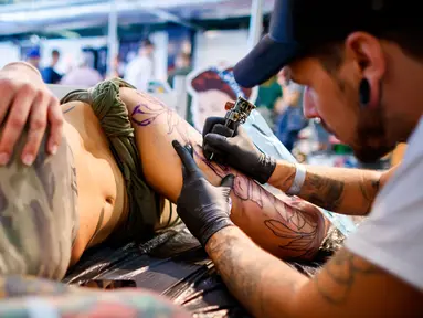 Seorang seniman mentato badan pengunjung wanita dalam acara edisi keempat Montreux Tattoo Convention di Montreux, Swiss  (22/9). Lebih 150 seniman tato dari 22 negara berkumpul dalam acara tersebut. (Valentin Flauraud/Keystone via AP)