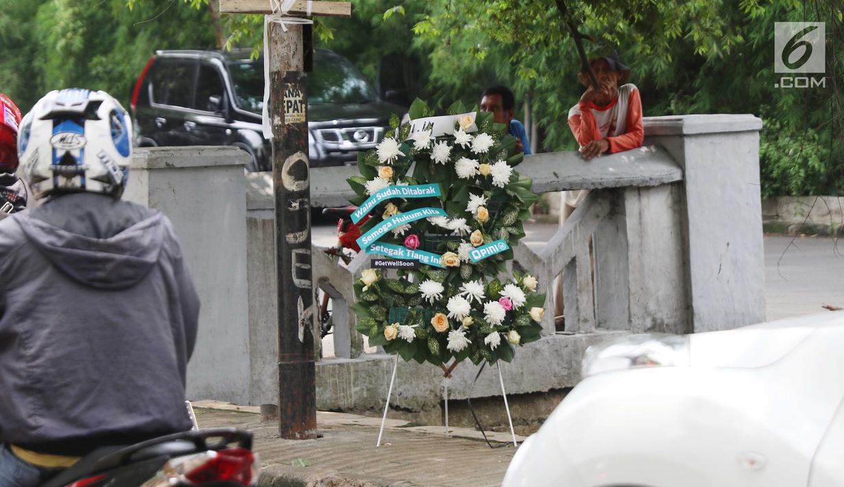 Warga berdiri dekat karangan bunga yang bersandar pada tiang lampu yang ditabrak mobil yang ditumpangi Ketua DPR Setya Novanto di Jalan Permata Berlian, Jakarta, Sabtu (18/11). Dalam karangan bunga tersebut tertulis pesan. (Liputan6.com/Angga Yuniar)