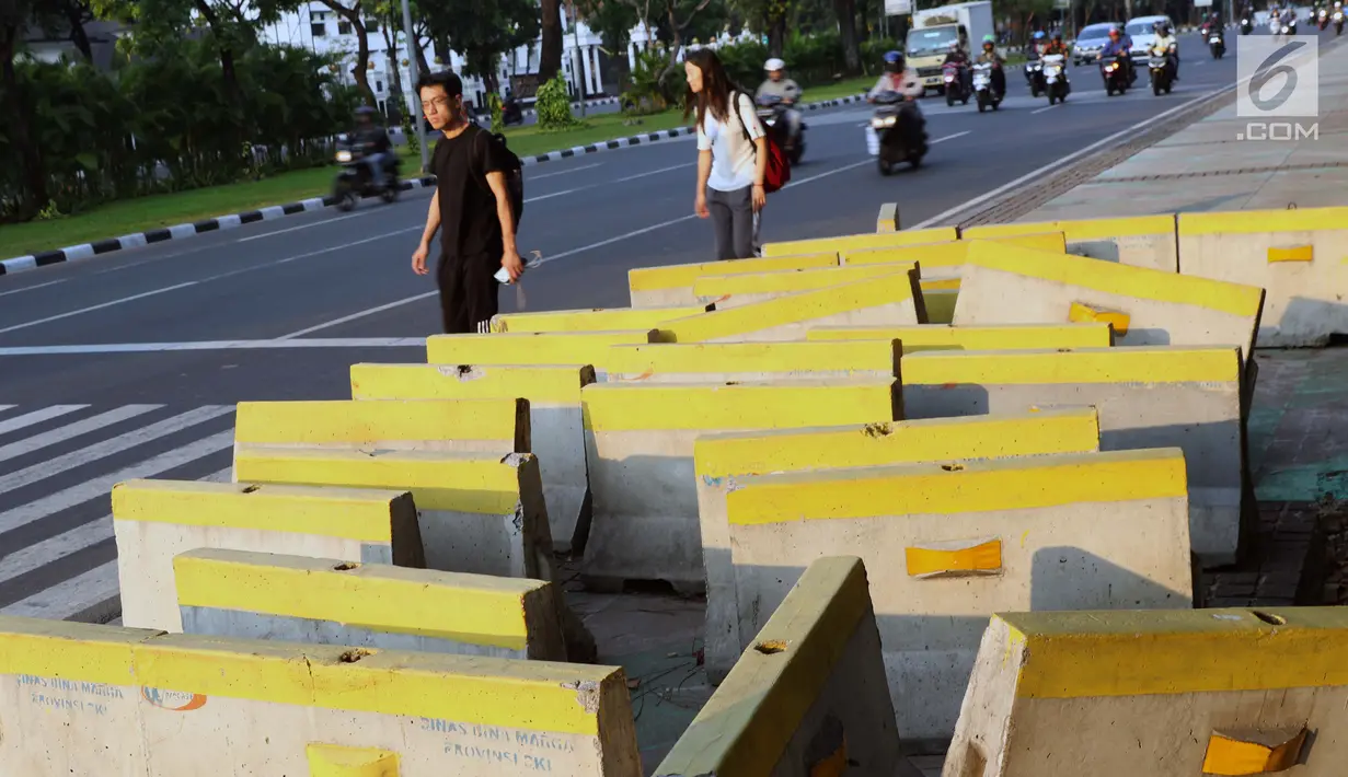 Pejalan kaki menghindari beton pembatas jalan yang diletakkan di atas trotoar Jalan Medan Merdeka Utara, Jakarta, Kamis (25/7/2019). Pembatas jalan yang berada tidak pada tempatnya mengganggu kenyamanan pejalan kaki yang melintasi trotoar jalan tersebut. (Liputan6.com/Helmi Fithriansyah)