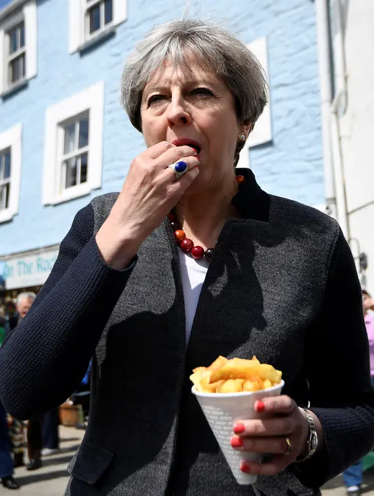 Perdana Menteri (PM) Inggris, Theresa May mencicipi beberapa keripik saat berhenti untuk kampanye di Mevagissey, Cornwall, Selasa (2/5). Theresa May melakukan kampanye dengan berkeliling jalanan di Cornwall. (AFP PHOTO/POOL/DYLAN MARTINEZ)