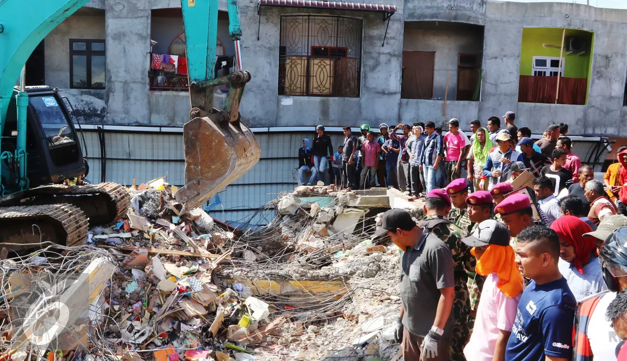 Warga melihat proses pengangkatan puing oleh eskavator di Pasar Meureudu yang hancur usai gempa, Pidie Jaya, Aceh, Kamis (8/12). Banyak bangunan di Aceh yang ambruk oleh gempa berkekuatan 6,4 SR. (Liputan6.com/Angga Yuniar)
