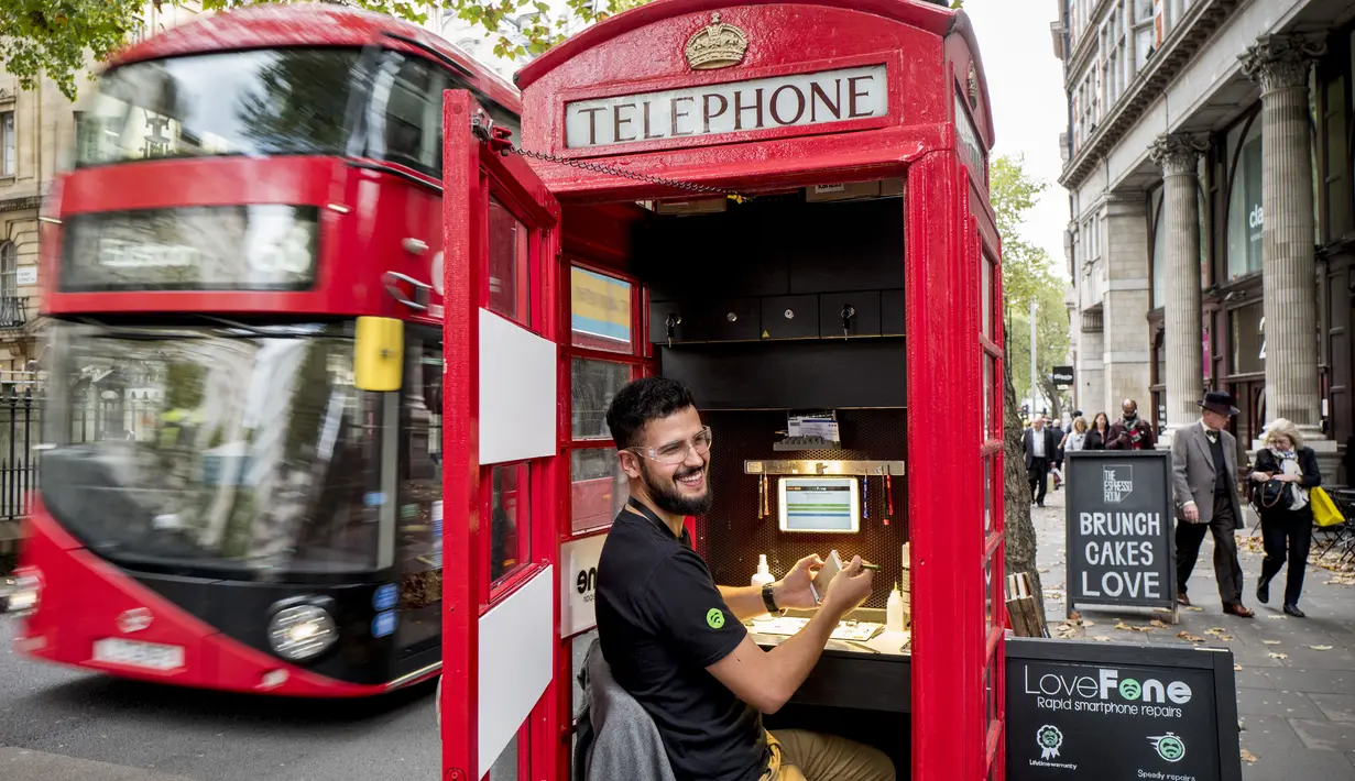 Seorang pria bernama Fouad Choaibi bekerja mereparasi ponsel didalam kotak telepon merah di Southhampton Row, London (20/10). Menjamurnya ponsel, membuat telepon umum di Inggris ini tidak beroperasi lagi. (AFP Photo/Tolga Akmen)