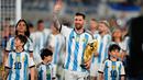 <p>Lionel Messi berjalan ditemani Antonela Roccuzzo dan anak-anak mereka dengan membawa trofi Piala Dunia sambil menyapa para penonton. (AP Photo/Natacha Pisarenko)</p>