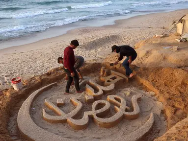 Warga membantu seniman Palestina, Yazeed Abu Jarad, saat ia membuat patung pasir dengan pesan ucapan "Selamat Datang, Ramadan" di sepanjang pantai di Khan Younis, selatan Gaza pada 17 Februari 2026. (Bashar Taleb/AFP)