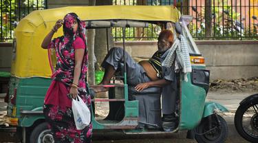 Seorang pengemudi bajaj yang kelelahan karena panas yang hebat beristirahat di dalam kendaraannya ketika seorang perempuan yang menutupi wajah berjalan melewatinya, di New Delhi, India, Kamis (19/5/2022). Meskipun hujan sporadis, ibu kota India itu masih menghadapi kondisi panas yang ekstrem. (AP Photo/Manish Swarup)
