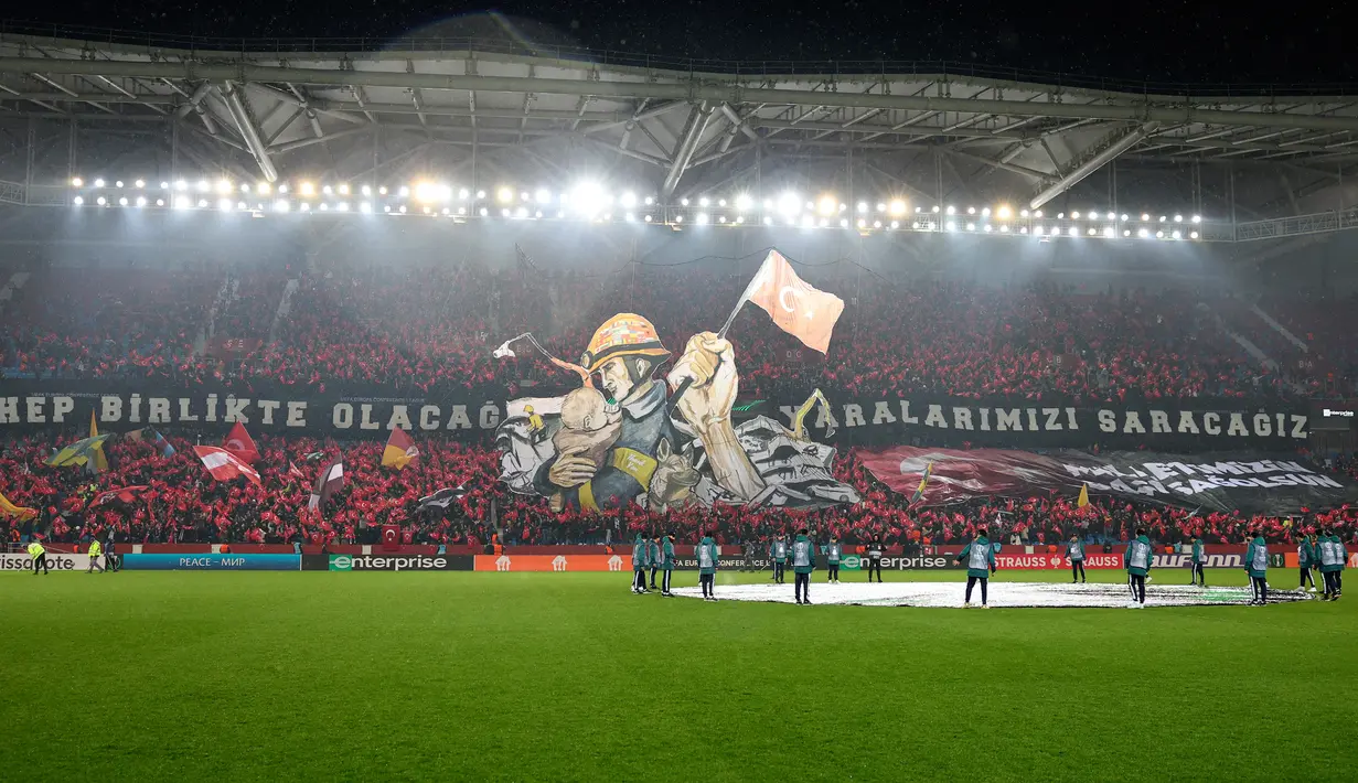 Fans menunjukkan gambar untuk menghormati korban gempa Turki dan Suriah sebelum dimulainya pertandingan sepak bola leg pertama playoff Liga Konferensi Eropa antara Trabzonspor dan Basel di Stadion Senol Gunes, Trabzon, Turki, 16 Februari 2023. (AP Photo)