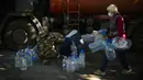 Pekerja mengisi ulang botol plastik dengan air di tempat penampungan untuk orang-orang yang terluka dan tunawisma di Izium, Ukraina, Rabu, 12 Oktober 2022. Dengan musim dingin yang semakin dekat, ada kekhawatiran serius tentang bagaimana orang akan bertahan hidup di suhu di bawah nol derajat tanpa panas. (AP Photo/Francisco Seco)