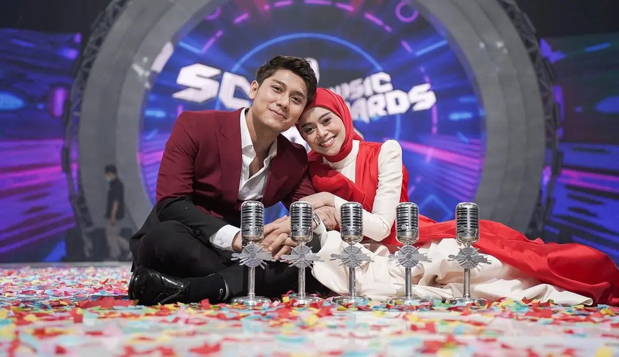 Rizky Billar menemani Lesti Kejora saat menerima penghargaan SCTV Music Awards. Keduanya kompak mengenakan baju atasan merah, sambil merangkul sang suami Lesti berpose di hadapan piala penghargaannya. (Foto: Instagram/@Lestykejora)