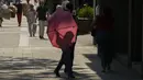 Seorang perempuan berjalan dengan payung untuk melindungi dari matahari di Madrid, Spanyol, Rabu (13/7/2022). Para pakar meteorologi mengatakan massa udara yang terlalu panas dan angin hangat dari Afrika mendorong suhu di kawasan Semenanjung Iberia naik melebihi suhu biasanya. (AP Photo/Paul White)