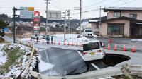 Sebuah kendaraan terparkir di tepi jalan yang runtuh di Kota Tohoku, Prefektur Aomori, Jepang, pada Selasa 9 Desember 2025. Gempa besar mengguncang lepas pantai utara Jepang. (JIJI Press/Japan OUT/AFP)