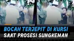 Seorang bocah laki-laki terjepit di kursi saat seorang perempuan dewasa tengah memeluk sang pengantin pria.