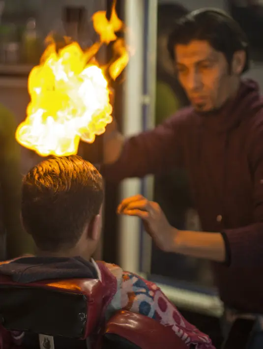 Api terlihat menyala di rambut seorang pelanggan di sebuah barbershop milik pria Palestina, Ramadan Edwan, di kamp pengungsian Rafah, di selatan Jalur Gaza, Rabu (1/2). Ramadan Edwan menggunakan api untuk mencukur rambut pelanggannya. (MAHMUD HAMS/AFP)