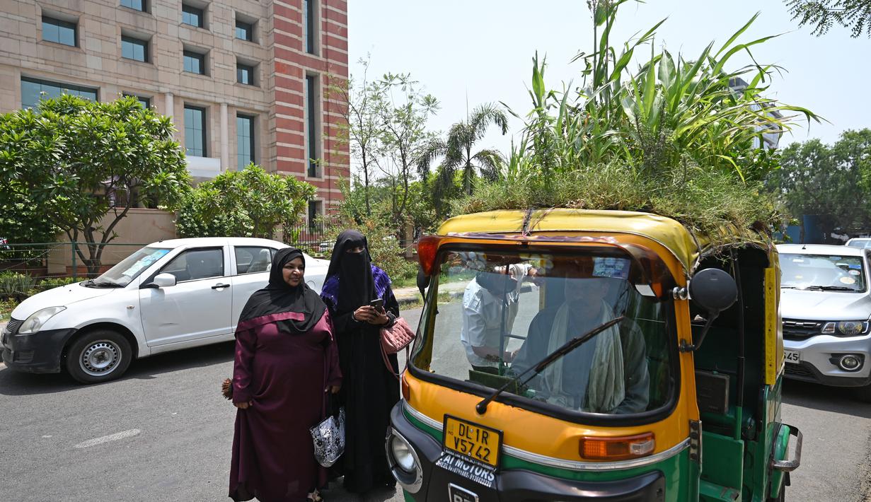 <p>Orang-orang berbicara dengan pengemudi bajaj Mahender Kumar&nbsp; saat ia duduk di kendaraannya dengan 'taman' di atapnya, di New Delhi, India pada 2 Mei 2022. Bajaj kuning dan hijau ada di mana-mana di jalan-jalan New Delhi tetapi kendaraan Mahendra Kumar sangat menonjol -- ia memiliki taman di atapnya bertujuan untuk menjaga penumpang tetap sejuk selama musim panas yang menyengat. (Money SHARMA / AFP)</p>