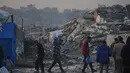 Fokus bantuan mencakup pengiriman pasokan medis ke fasilitas kesehatan yang tersisa serta peralatan untuk perbaikan layanan air dan sanitasi guna mencegah krisis penyakit. Tampak dalam foto, warga Palestina berjalan melewati perkemahan tenda di tengah bangunan-bangunan yang hancur akibat serangan udara dan darat Israel di Kota Gaza, Selasa 6 Januari 2026. (AP Photo/Jehad Alshrafi)